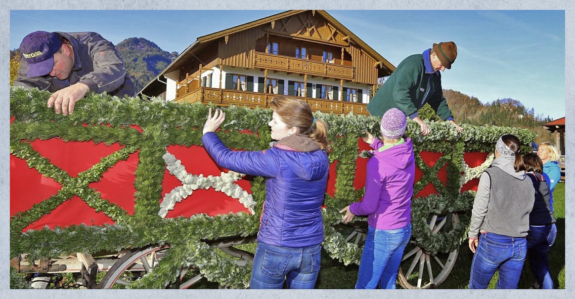 Fünf Frauen und zwei Männer schmücken ein Leonhardi-Fuhrwerk. Im Hintergrund ein großes Bauernhaus.